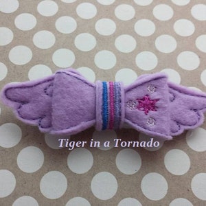 Peut inclure: Noeud en feutre violet avec une étoile rose et des rayures bleues et violettes. Le noeud est en forme d'ailes et porte l'inscription "Tiger in a Tornado".
