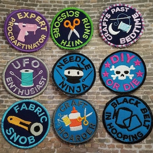 Könnte beinhalten: Neun gestickte Bügelbilder mit verschiedenen Bastelmotiven. Die Patches sind rund und zeigen farbenfrohe Designs mit Texten wie "Expert Procrastinator", "UFO Enthusiast", "DIY or Die", "Craft Hoarder" und "Black Belt in Hooping".