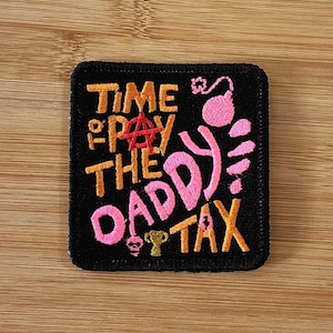 Peut inclure: Un écusson carré brodé noir avec le texte orange TIME TO PAY THE DADDY TAX, un symbole anarchiste rouge, une icône de bombe rose, un petit crâne rose et une icône de trophée doré. La broderie est réalisée avec des fils aux couleurs vives.