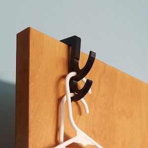 May include: Two black over-the-door hooks with a blue and purple tie-dye shirt, a red and blue paisley scarf, and a red robe hanging on them.
