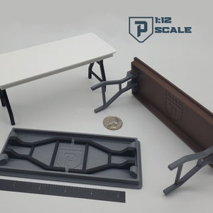 May include: A set of three 1:12 scale folding tables in white, brown, and gray. The tables are made of plastic and have a simple design. The tables are folded up and ready to be stored.