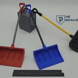 Könnte beinhalten: Drei Miniaturschaufeln in Rot, Blau und Schwarz mit grauen, gelben und schwarzen Griffen. Die Schaufeln lehnen an einer grauen Kiste. Ein Lineal befindet sich unten. Der Text "1:6 SCALE" ist sichtbar.