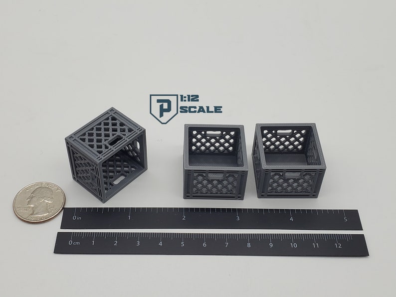 Puede incluir: Tres cajas de leche de pl&aacute;stico gris, cada una mide aproximadamente 5 cm de ancho, est&aacute;n dispuestas sobre una superficie blanca. Una regla se coloca debajo de las cajas, con marcas en pulgadas y cent&iacute;metros.