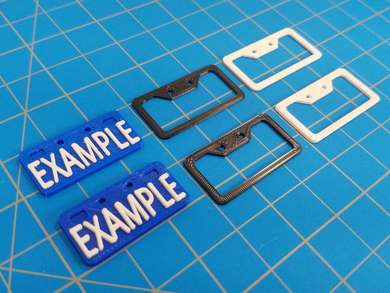 Puede incluir: Cuatro marcos para placas de matr&iacute;cula, dos negros y dos blancos, con dos placas de matr&iacute;cula azules que dicen "EXAMPLE" en letras blancas.
