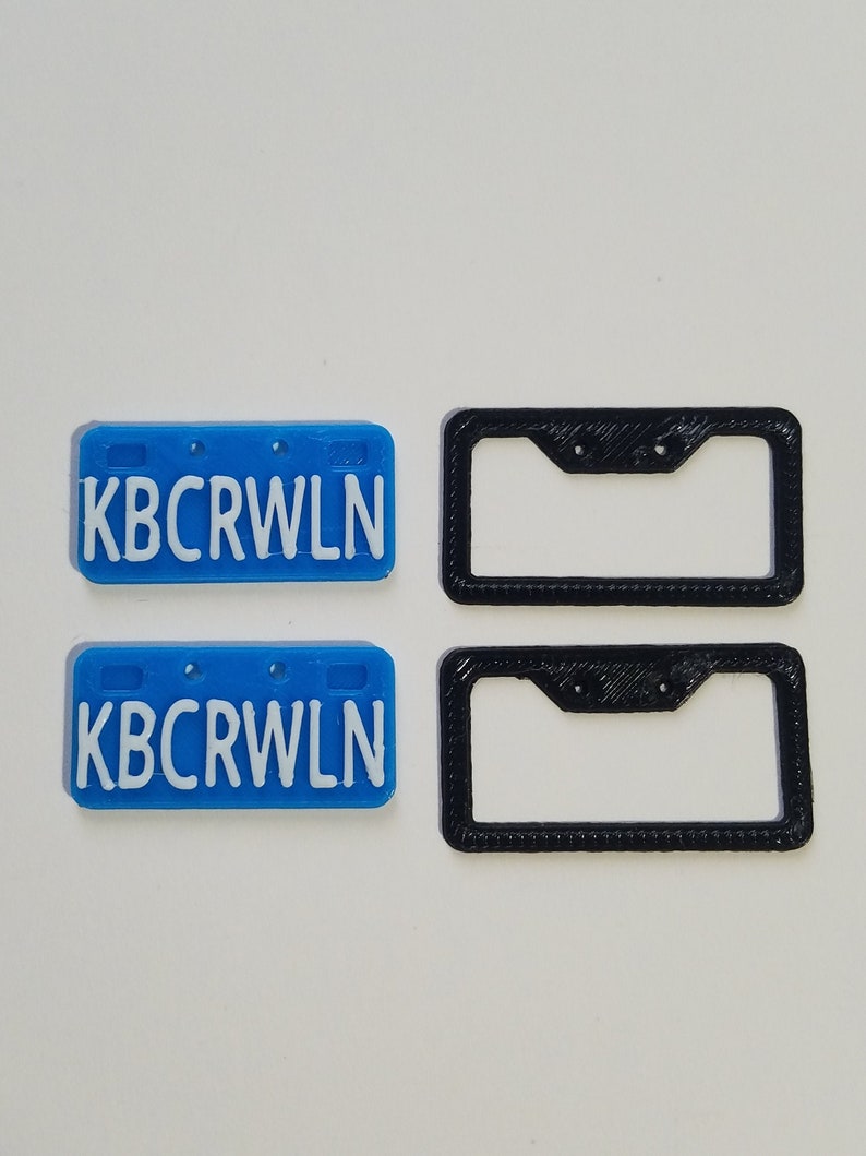Puede incluir: Dos placas de matr&iacute;cula de pl&aacute;stico azul con el texto "KBCRWLN" en letras blancas. Dos marcos de matr&iacute;cula de pl&aacute;stico negro.