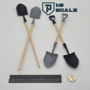 May include: Four miniature shovels with wooden handles and gray or black shovel heads are crossed in pairs. The image also includes a ruler, a coin, and the text "1:6 SCALE" in a logo.