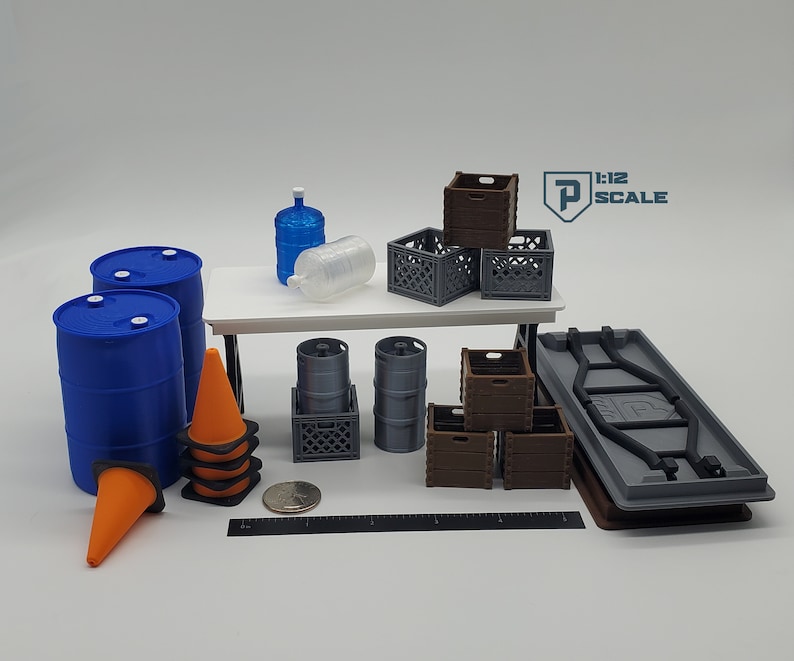 K&ouml;nnte beinhalten: Eine Sammlung von Miniatur-Requisiten f&uuml;r den Modellbau, darunter zwei blaue F&auml;sser, zwei graue F&auml;sser, zwei orangefarbene Verkehrskegel, eine graue Pritsche, ein Stapel brauner Holzkisten, ein Stapel grauer Plastikkisten und zwei durchsichtige Plastikwasserflaschen.