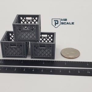 Puede incluir: Tres cajas de leche de pl&aacute;stico gris apiladas una encima de la otra. Las cajas miden aproximadamente 5 cm de alto y est&aacute;n sobre una regla negra. La regla est&aacute; marcada en pulgadas y cent&iacute;metros. Una moneda de 25 centavos de d&oacute;lar estadounidense de plata est&aacute; junto a las cajas.