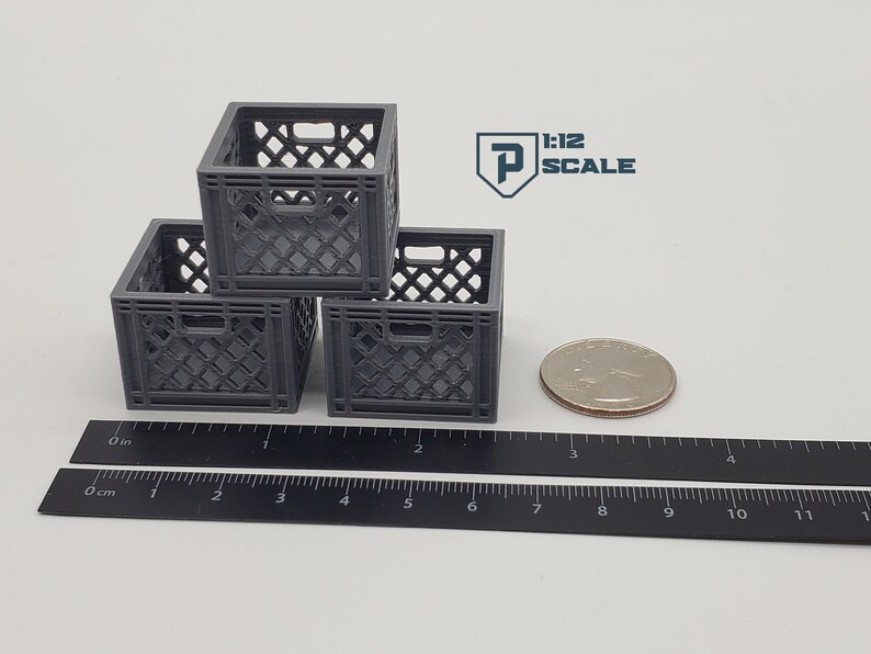 Puede incluir: Tres cajas de leche de pl&aacute;stico gris apiladas una encima de la otra. Las cajas miden aproximadamente 5 cm de alto y est&aacute;n sobre una regla negra. La regla est&aacute; marcada en pulgadas y cent&iacute;metros. Una moneda de 25 centavos de d&oacute;lar estadounidense de plata est&aacute; junto a las cajas.