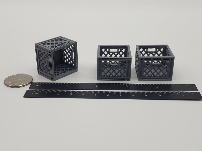 Puede incluir: Tres cajas de leche de pl&aacute;stico gris, cada una mide aproximadamente 5 cm de alto, est&aacute;n dispuestas sobre una superficie blanca. Una regla se coloca debajo de las cajas para la escala.