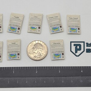 May include: Miniature seed packets for various vegetables, including radish, pumpkin, onion, peppers, tomato, romaine lettuce, purple broccoli, and watermelon. A quarter coin and a ruler are included for scale. The text "1:6 SCALE" is also visible.