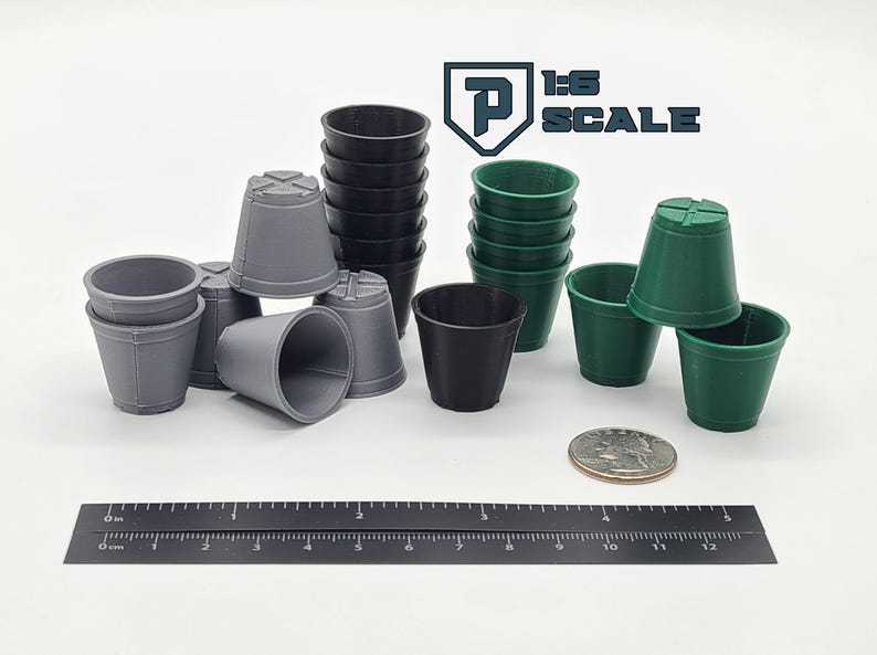 May include: A collection of small, plastic plant pots in various colors: gray, black, and green. A ruler with inch and centimeter markings is placed next to the pots. The text "1:6 SCALE" is visible in the upper right corner.