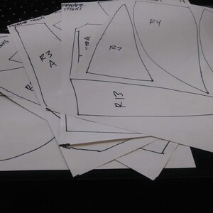 May include: A set of white paper sewing patterns with handwritten labels and numbers, including "Predator Thighs", "R3 A", "TOA", "R13", "R7", "R4", and "R1".