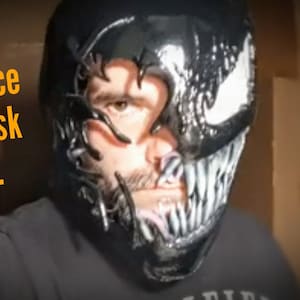 May include: A black and white Venom mask worn by a person. The mask is made of plastic and features a detailed design. It covers the wearer's face from forehead to chin.