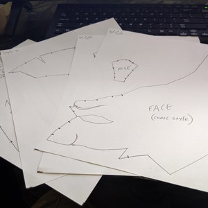 May include: Three pieces of paper with black ink drawings of a face, nose, and part of a pattern. The paper is labeled "W/C/K" and "FACE (comic style)".