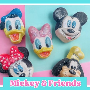 Könnte beinhalten: Eine Sammlung von Figuren in Form von Charakteren mit Micky Maus, Donald Duck, Daisy Duck, Minnie Maus und Goofy. Die Artikel sind farbenfroh mit Glitzerakzenten und vor einem rosa-blauen Hintergrund platziert. Der Text "Mickey & Friends" befindet sich unten.