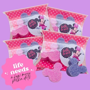 May include: Mickey Mouse-shaped bath bombs in pink and purple with glitter, presented in clear bags with a pink polka dot pattern. Each bag features a label with Minnie Mouse and the words "bath bomb". The image also includes the text "life needs a few more polka dots".