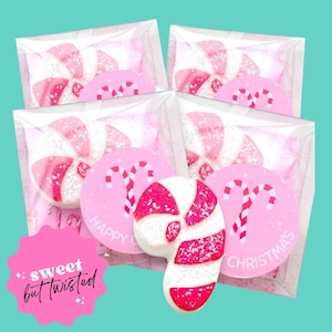 Könnte beinhalten: Vier transparente Verpackungen mit rosa und weiß wirbelnden Süßigkeiten, mit rosa runden Aufklebern mit einem Zuckerstangenmuster und der Aufschrift "Happy Christmas". Eine rosa, weiße und rote Zuckerstange befindet sich davor. Der Text "sweet but twisted" steht auf einem rosa Stern.