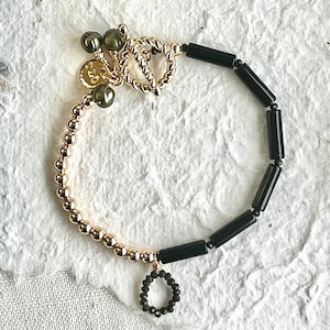 May include: A gold bracelet with black beads and a gold clasp. The bracelet has a small charm with a circle of black beads.