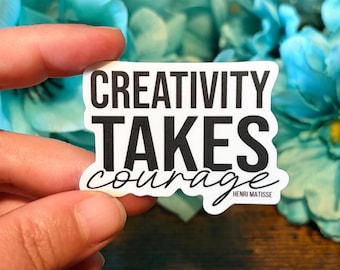 May include: A white sticker with the words "CREATIVITY TAKES courage" in black, with "HENRI MATISSE" in small print. The sticker is held against a backdrop of blue flowers.