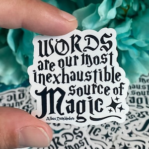 Op de afbeelding: Een witte sticker met zwarte tekst in gotische letters. De tekst luidt: "WORDS are our most inexhaustible source of Magic". De naam "Albus Dumbledore" staat er ook op. De sticker heeft een decoratieve vorm.