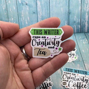 May include: A sticker with the text "THIS WRITER runs on Creativity and Tea" with a tea bag tag. The sticker is white with green and purple accents.
