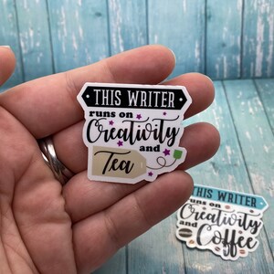 May include: A white sticker with black text that reads "This Writer runs on Creativity and Tea". The sticker features a brown tea bag with a white string and a green tag. The sticker has purple stars around the text.