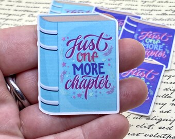 May include: A blue book sticker with the text "Just one more chapter" in pink and purple lettering. The sticker has a white border and a glittery background.