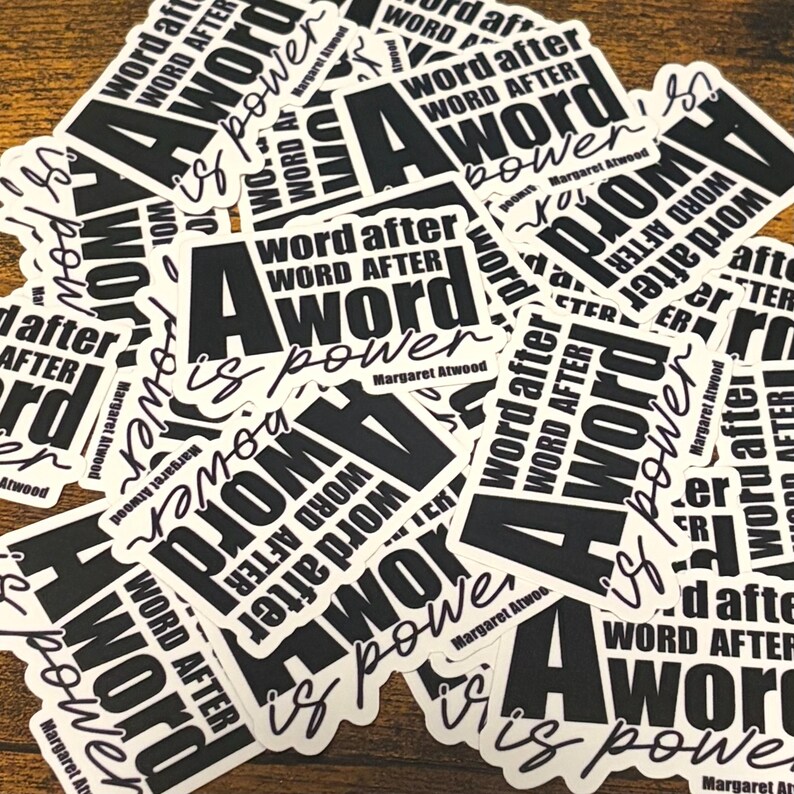 May include: A collection of white stickers with black text. Each sticker features the quote "A word after word is power" by Margaret Atwood. The design includes a large letter "A" and the quote in a bold, readable font.