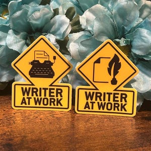 Peut inclure: Deux autocollants jaunes en forme de losange avec des bordures noires et le texte "Writer at Work". Un autocollant représente une machine à écrire avec une feuille de papier. L'autre autocollant représente une plume et une feuille de papier.