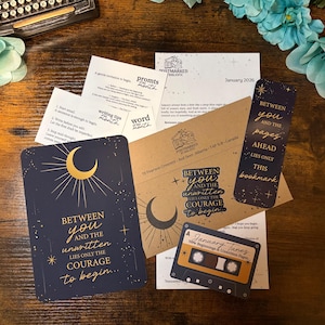 May include: A selection of stationery items, including cards, a bookmark, and an envelope, with celestial and literary themes. The cards feature crescent moon designs and the text "Between you and the unwritten lies only the courage to begin..."