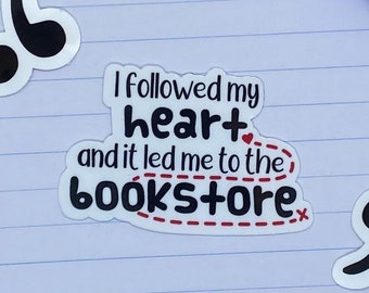 May include: A white sticker with the text "I followed my heart and it led me to the bookstore" in black and red. The word "heart" has a small red heart. The sticker is on a lined paper background.