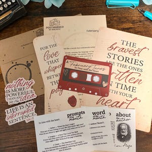 May include: A collection of stationery items with a literary theme. Includes cards with quotes, a cassette tape design, and the text "February Tunes In Time with the Heart." Also features a typewriter and pen.