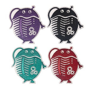 May include: Four embroidered iron-on patches featuring a cartoon creature with a segmented body, resembling a pill bug or a trilobite. The patches are in purple, black, teal, and red.