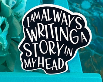 Può includere: Adesivo bianco e nero con il testo "I am always writing a story in my head". L'adesivo ha la forma di una testa ed è su uno sfondo blu.