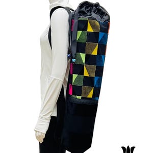 May include: Black yoga mat bag with a geometric pattern in shades of blue, green, yellow, and pink. The bag has a drawstring closure and a shoulder strap. The bottom of the bag is black velvet.