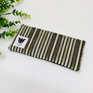 May include: A striped eye pillow in brown and beige. The pillow features vertical stripes and a white label with a black tulip logo and the text "MY YOGA ROOM ELEMENTS". This pillow is designed for relaxation and meditation, measuring approximately 20 cm in length.