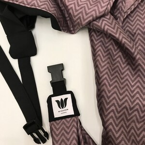May include: A black and gray baby carrier with a zig-zag pattern. The carrier has a black strap with a buckle and a white label that says "My Yoga Room".