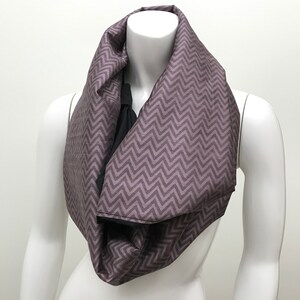 May include: A purple and black infinity scarf with a chevron pattern.