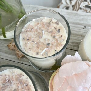 May include: A close-up of a white candle with a clear glass jar. The candle is topped with small, glittery, pink and silver pieces.