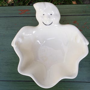 May include: White ceramic ghost shaped bowl with a smiling face. The bowl is perfect for holding candy or other small treats.
