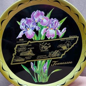 Könnte beinhalten: Ein rundes Tablett aus Metall in Schwarz und Gold mit einer Karte von Tennessee und der Staatsblume, der Iris, in der Mitte. Das Tablett trägt den Text "Tennessee" und "IRIS STATE FLOWER".