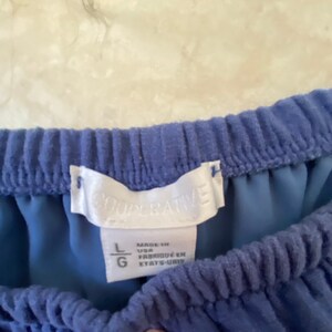 May include: A blue off-the-shoulder top with a white tag that says "COOPERATIVE" and size "L". The tag also says "Made in USA" and "Fabriqu&eacute; en &Eacute;tats-Unis".