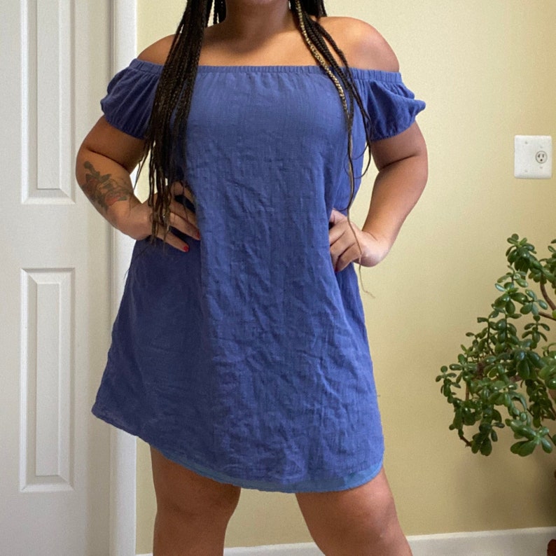 May include: A blue off-the-shoulder dress with a loose fit and a slightly ruffled neckline.