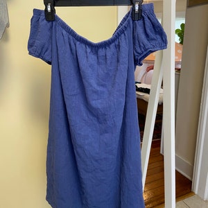 May include: A blue off-the-shoulder dress with short sleeves. The dress is made of a soft, textured fabric.