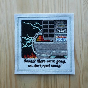 May include: Embroidered patch featuring a silver DeLorean time machine with flames and lightning bolts. The text "Roads? Where we're going, we don't need roads!" is below the image.