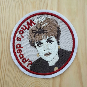 May include: Embroidered patch with a red border and white backing. The patch features a woman with brown hair and a white shirt, with the text "Who's dead?" in red.