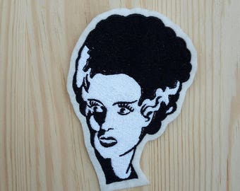 Può includere: Toppa ricamata in bianco e nero con il viso di una donna con un'acconciatura che ricorda quella di Frankenstein.