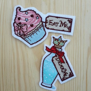 Può includere: Due toppe da stirare ricamate con temi di Alice nel Paese delle Meraviglie. Una toppa è un cupcake rosa con una base blu e un'etichetta che dice "Mangia me". L'altra toppa è una bottiglia blu con una corona e un'etichetta che dice "Bevi me".