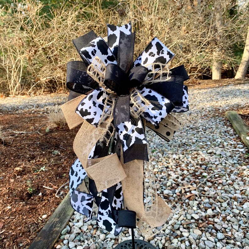 Black and White Cow Bow on a wreath stand photographed outdoors to give a natural light perspective.  The wreath stand is for display only and not for sale. Refer to the listing description for further bow details.